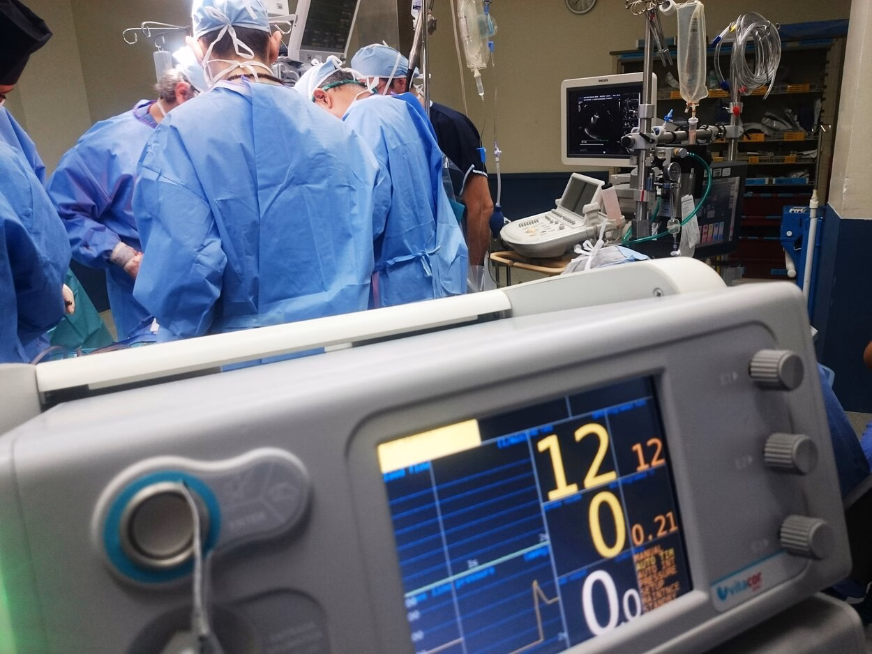 Doctors are working in an operating room in blue coats.