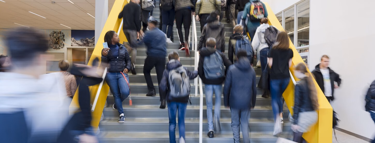 Middle school students walk up the stairs in the hall of their school.