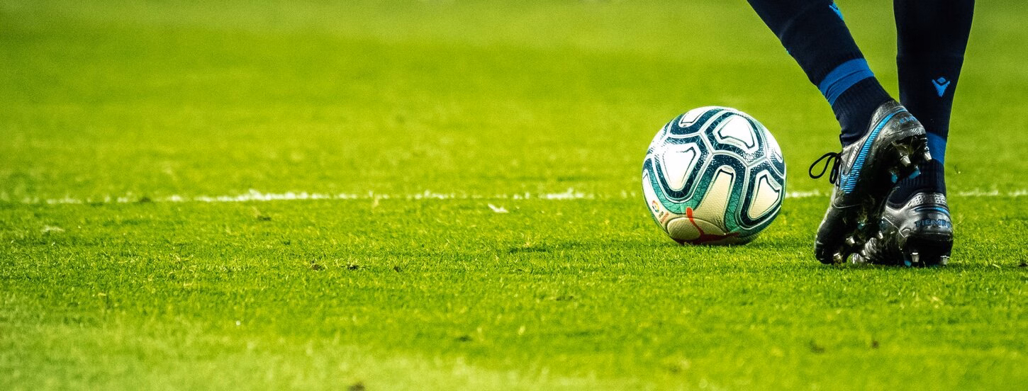 Soccer player walking with ball across soccer field