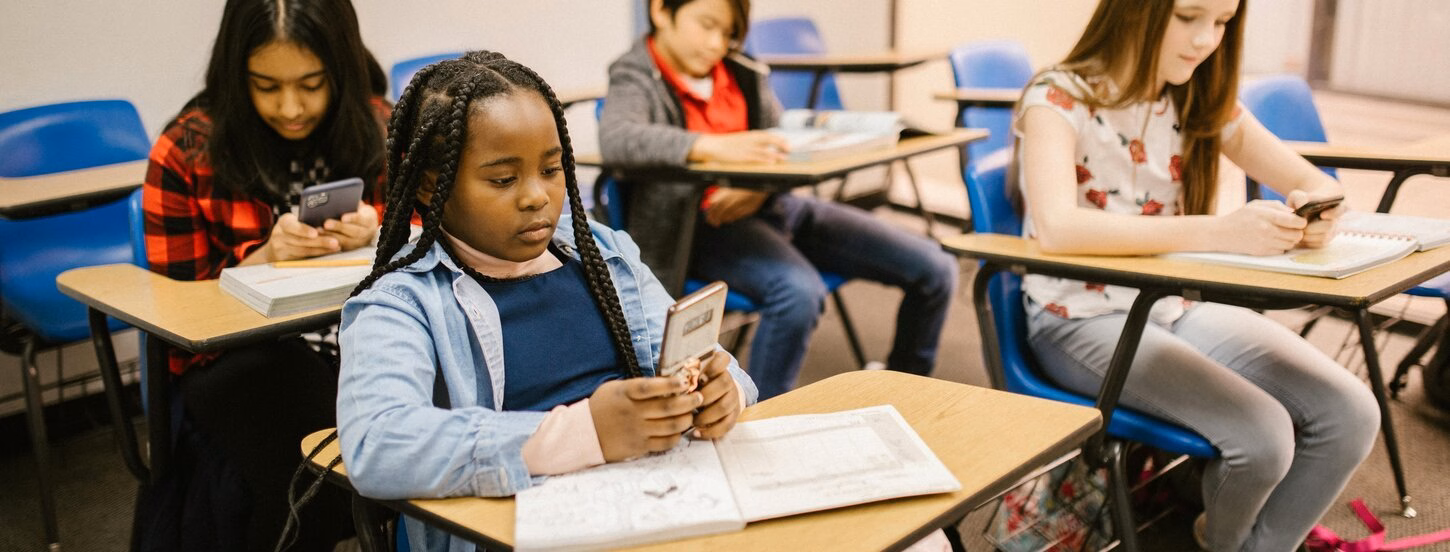 Vier schoolkinderen gebruiken hun telefoon in het klaslokaal