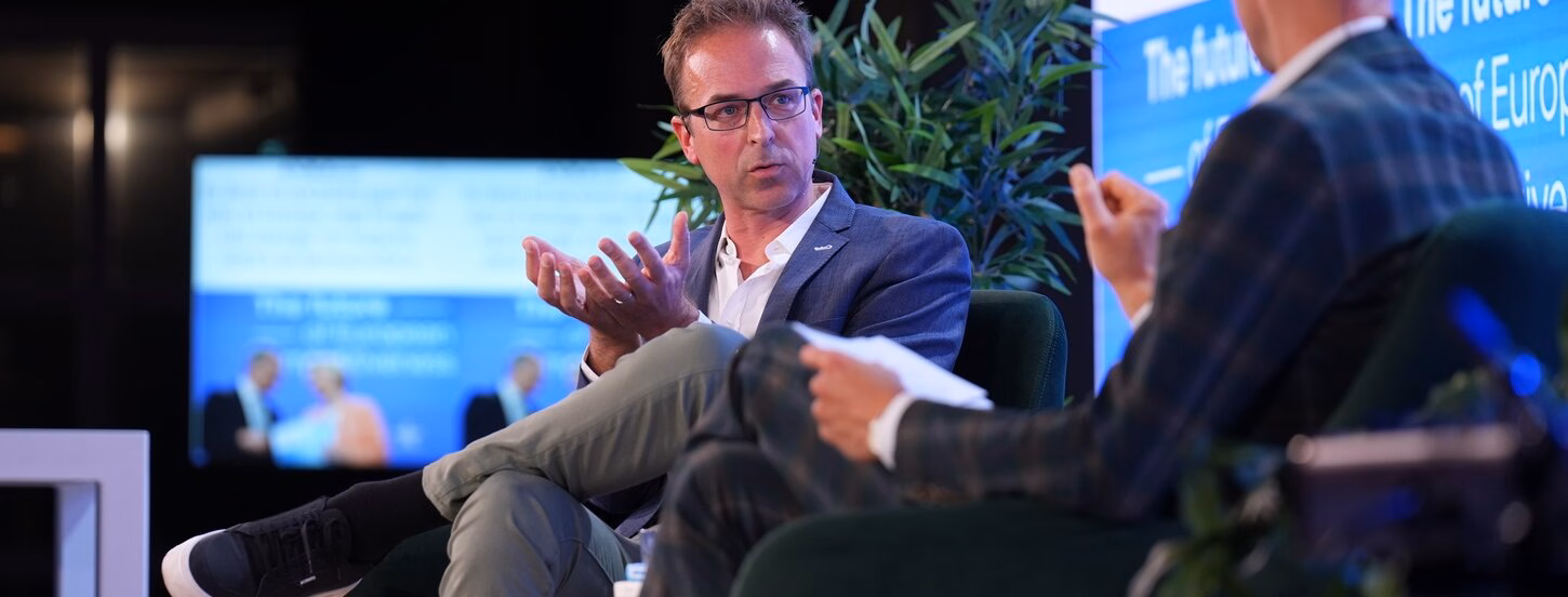Men sitting with one leg on top of the other while making a gesture with his hands and the side profile of a man