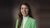 Smiling woman in a green blazer and white turtleneck against a brown backdrop.