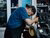 Mechanic in cap and overalls using a power polisher on a car body panel in garage