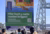 People seated by harbor crane facing large Dutch sign with wave illustration and QR code