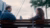 Een man en een vrouw in gesprek op een bankje bij de waterkant, met op de achtergrond de skyline van Rotterdam bij bewolkt weer.