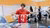 Person holding up scrapes of clothes, in the background more people working with fabric