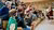 Children in stands with headphones on and hands in the air to ask questions