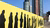 Yellow fence with black silhouettes of queued people against city skyscrapers