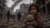 Young child clutching teddy bear amid rubble of bombed-out city with smoke and planes overhead