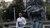 Man in white shirt holding folders stands next to bronze scholar statue on plaza