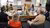 Acht collega’s zitten rond een ovale tafel in een zonovergoten kantoor en zijn in gesprek terwijl ze met hun laptops en documenten bezig zijn.