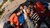 Seven friends in colorful jackets leaning over shiny sculpture, smiling up at camera