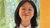 Young woman with glasses smiling before a yellow pillar and green foliage