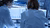 Researchers in white lab coats studying scan images on dual screens in blue-lit lab