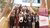 Group of about 40 people posed on a wooden staircase in a modern atrium beside a banner