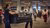 Two men carrying a black couch through a busy airport terminal