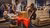 Woman lifting red cushions beside couch in busy warehouse full of furniture