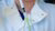 Scientist in white lab coat pipetting green liquid into Erlenmeyer flask