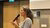 Photograph of a woman speaking into a microphone at a wooden podium in a lecture hall