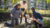 Photograph of three people kneeling in urban community garden, planting a young sapling