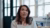Woman in a light sweater sits in a bright office, gazing upward thoughtfully.